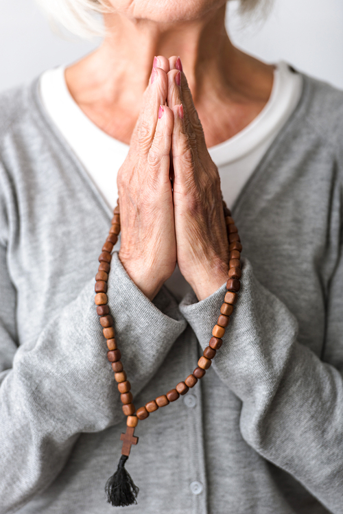 partial view of senior woman praying with wooden rosary