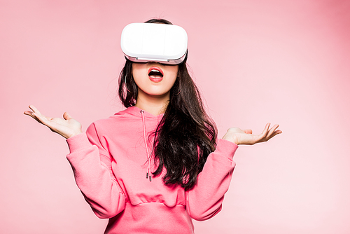 shocked woman in pink pullover with virtual reality headset isolated on pink