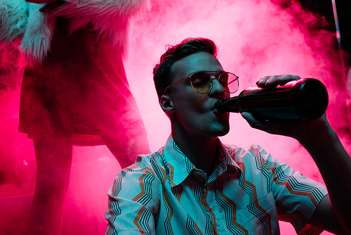 handsome man in sunglasses drinking alcohol during rave in nightclub