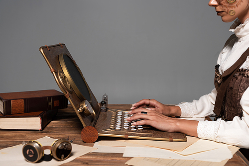 cropped view of woman typing on steampunk laptop at table isolated on grey
