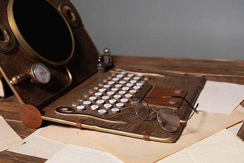 steampunk laptop, glasses and documents on wooden table isolated on grey