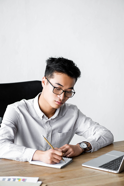 asian seo manager writing in notebook during webinar in office