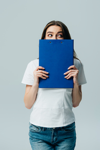 beautiful girl in white t-shirt holding blue clipboard in front of face and looking away isolated on grey