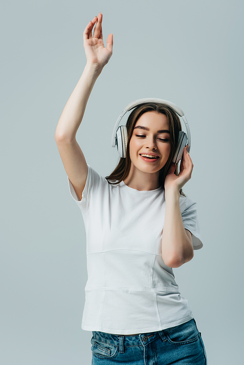 happy pretty girl listening music in wireless headphones and dancing isolated on grey