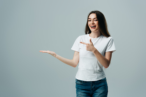 beautiful excited girl pointing with hand and finger at copy space isolated on grey