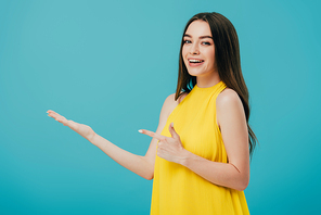 happy beautiful girl in yellow dress pointing with finger at copy space isolated on turquoise