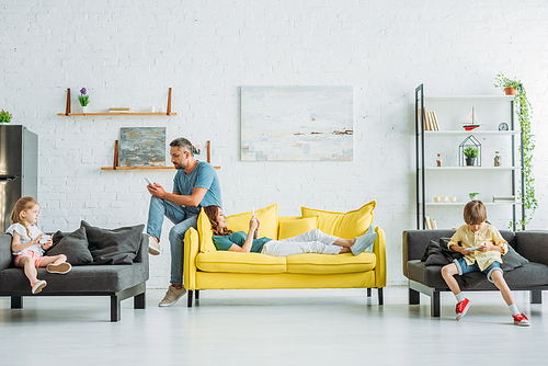 mother and father with two children using smartphones while resting on couches at home