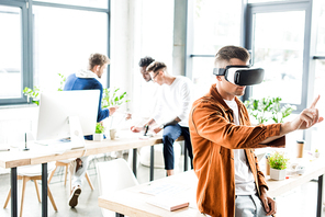 young businessman using vr headset and touching something with finger while multicultural colleagues working in office