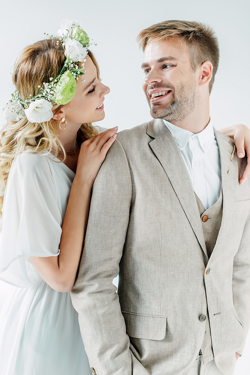 attractive bride and handsome bridegroom smiling and looking at each other isolated on grey