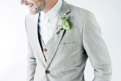 cropped view of smiling bridegroom in suit with boutonniere isolated on grey