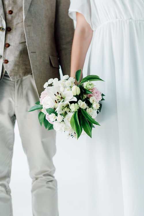 cropped view of bride with bouquet and bridegroom in suit