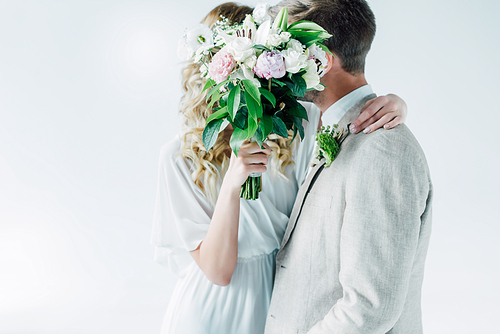 bride in wedding dress and bridegroom hugging and holding bouquet