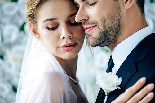 attractive bride and handsome bridegroom hugging with closed eyes