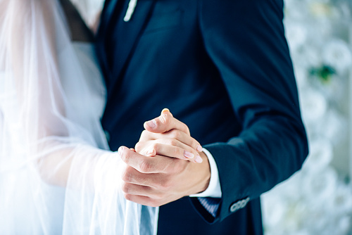 cropped view of bride in wedding dress and bridegroom holding hands