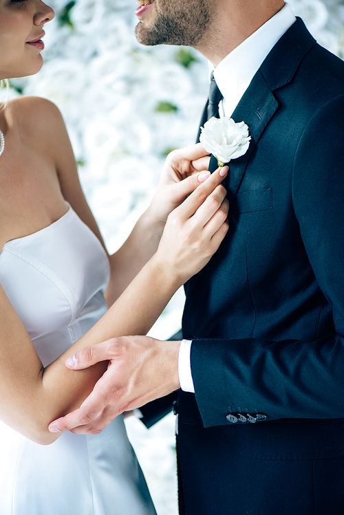 cropped view of bride in wedding dress holding buttonhole of her bridegroom