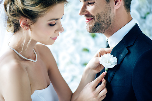 attractive bride in wedding dress holding buttonhole of her bridegroom