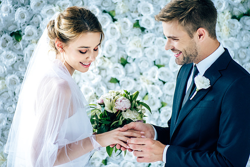 handsome and smiling  bridegroom putting wedding ring on finger