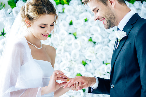 attractive and smiling bride putting wedding ring on finger