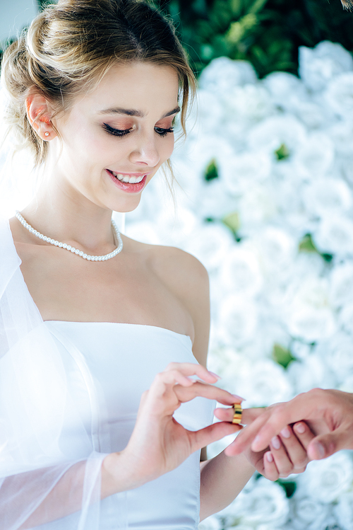 attractive and smiling bride putting wedding ring on finger