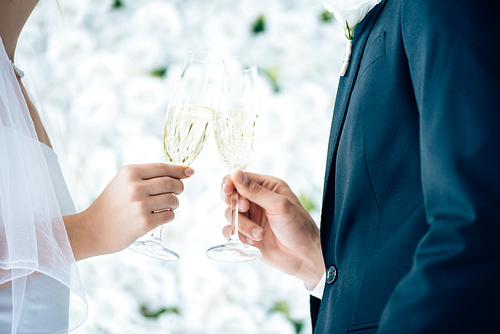 cropped view of bride and bridegroom clinking with champagne glasses