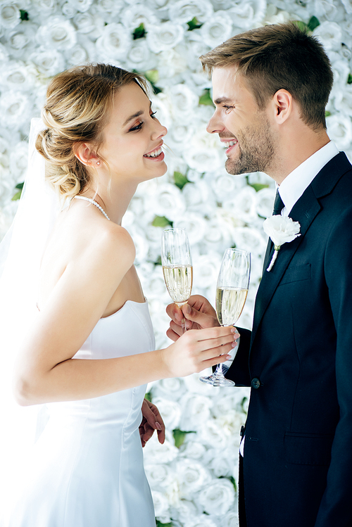 attractive bride and handsome bridegroom smiling and clinking with champagne glasses