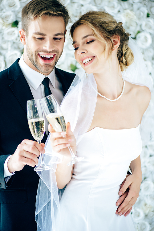 attractive bride and handsome bridegroom smiling and clinking with champagne glasses