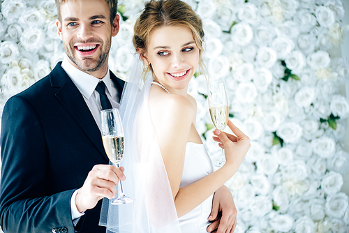 attractive bride and handsome bridegroom smiling and holding champagne glasses