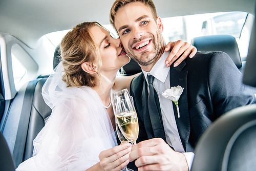 attractive bride and handsome bridegroom kissing and clinking with champagne glasses