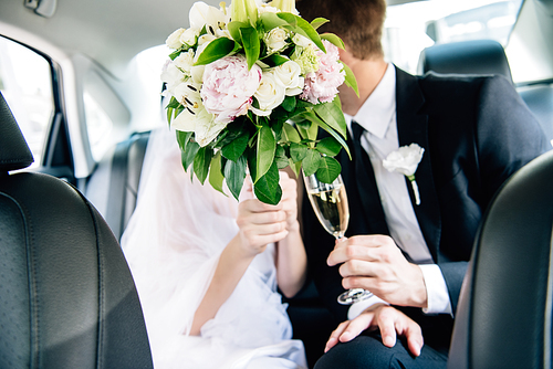 selective focus of bridegroom in suit and bride holding bouquet