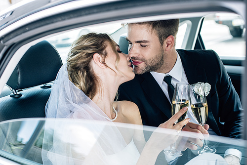 attractive bride and handsome bridegroom kissing and clinking with champagne glasses