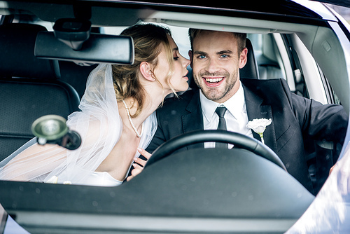 attractive bride in bridal veil kissing handsome bridegroom in car