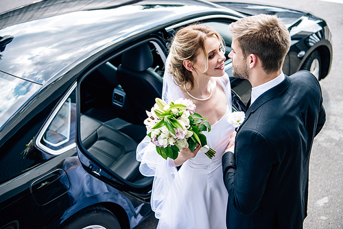 bridegroom in suit kissing attractive and blonde bride with bouquet