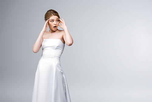 shocked girl in wedding dress looking away and touching temples isolated on grey
