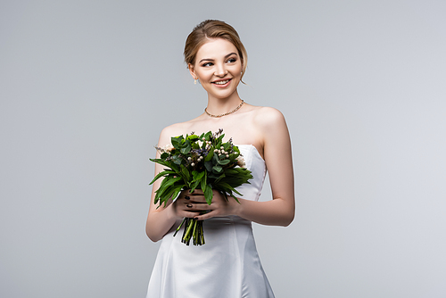 happy bride in white dress holding wedding flowers isolated on grey
