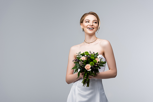 positive girl in white dress holding wedding flowers isolated on grey