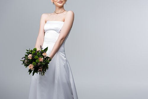 cropped view of bride in white wedding dress holding flowers isolated on grey