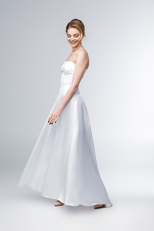 smiling bride in elegant wedding dress standing on grey