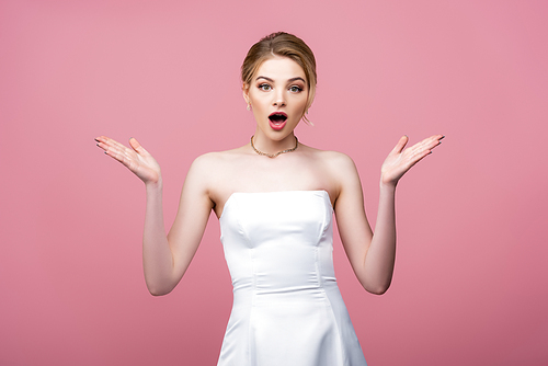 surprised bride in white wedding dress gesturing isolated on pink