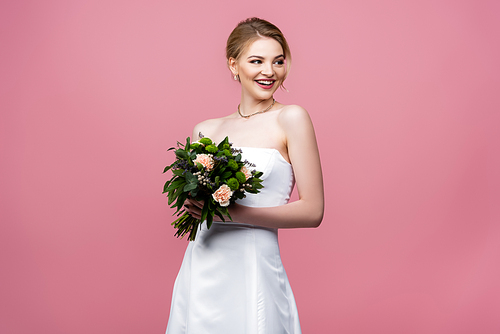 smiling bride in white wedding dress holding flowers isolated on pink