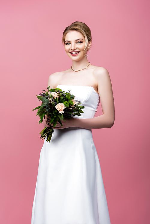 happy girl in white wedding dress holding flowers isolated on pink