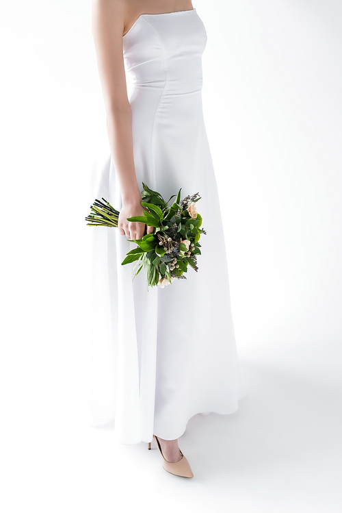 cropped view of bride in elegant wedding dress holding flowers on white