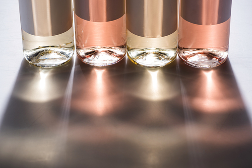 close up view of bottles of white and rose wine with blank labels on grey background with light