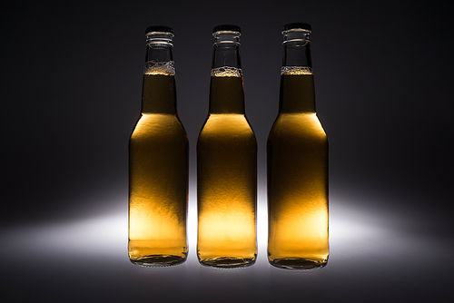 three glass bottles with beer on black background with back light