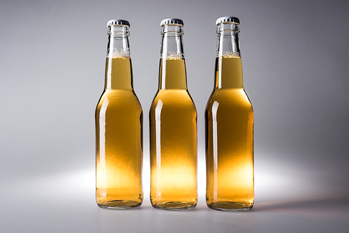 three glass bottles with beer on grey background