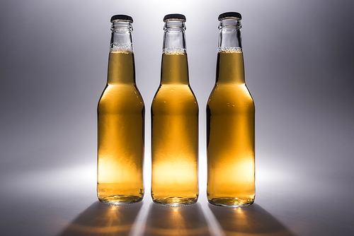 three glass bottles with beer on grey background with back light