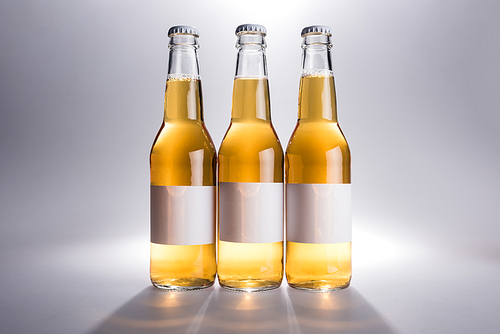 three glass bottles with beer with white labels on grey background