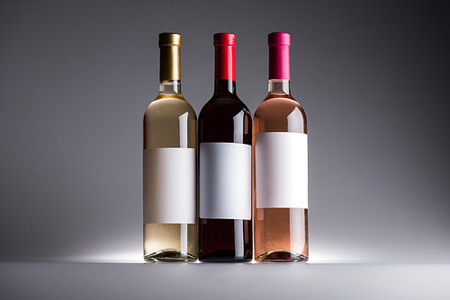 bottles of red, white and rose wine with blank labels on dark background with back light