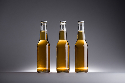 three glass bottles with beer in row on grey background