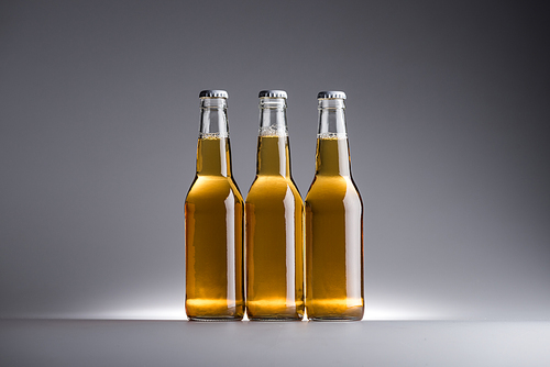 three glass bottles with beer in row on grey background with copy space