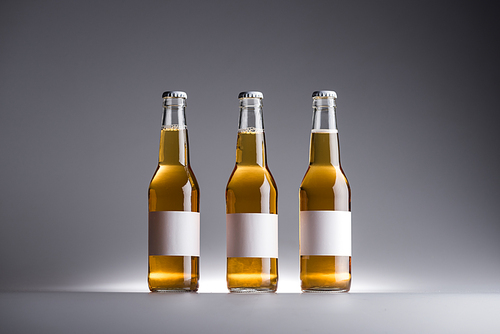 three glass bottles with beer in row with white labels on grey background